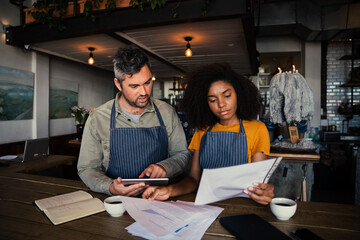 Worried male and female co-worker looking at finances in authentic coffee shop.