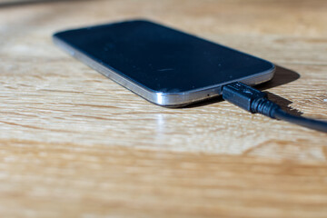 Mobile smartphone charging on a wooden by sharing energy via a power bank. Tech Device Charge Sharing. Sharing technology device charge. White-colored power bank charging the black color smartphone.