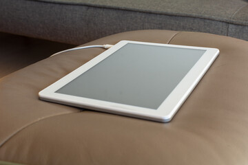A white tablet charging energy on the sofa. blur background with copy space