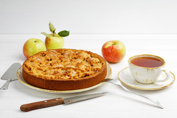 Fresh baked homemade apple and cinnamon pie and cup of tea on white wooden table.
