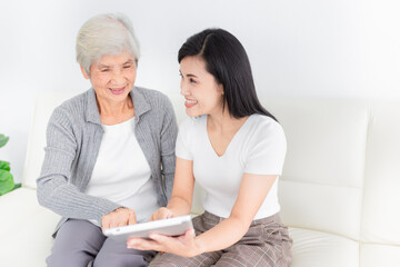 young Asian female and old female search information with tablet computer, they feeling happy and smile, they sitting on sofa, mother's day and happiness family time, technology and social network