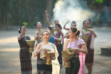 Group of beautiful Asian women in traditional costumes splashing water in Songkran Festival at...