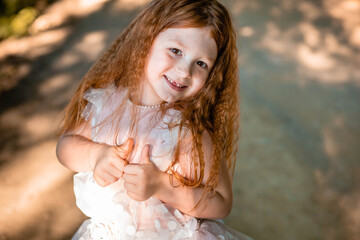 Adorable, ginger little girl smiles and shows thumbs up