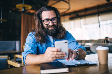 Long haired bearded man chatting on smartphone in cafe
