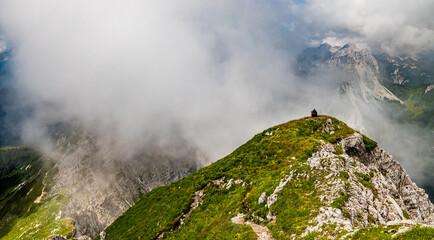 Young woman summer hiker backpack resting on hill steep slopes, panoramic mountains with cloudy fog valleys. Female trekker in challenging terrain Karavanke, Slovenia Karawanken, Carinthia, Austria