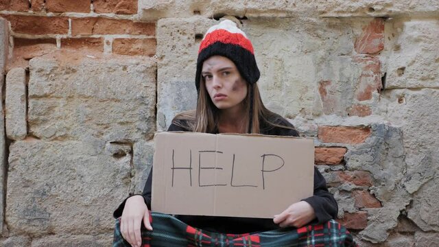 A homeless girl in a hat sits on the sidewalk and asks for help outdoors. Indifference to homeless people. Hand help.