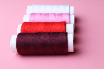 Accessories for sewing. Colored spools of thread on a pink background.