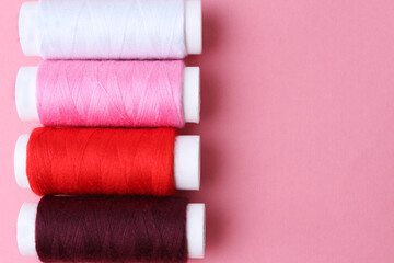 Accessories for sewing. Colored spools of thread on a pink background.