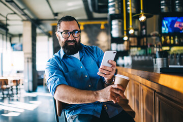 Man with smartphone and cup of hot drink in bar