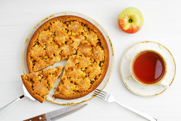 Fresh baked homemade apple and cinnamon pie and cup of tea on white wooden table. Top view.