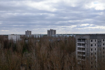 Fototapeta na wymiar Abandoned panel houses among leafless trees in Pripyat. Beautiful cloudy sky over the city. Post-Soviet architecture.