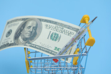 buying a thermometer. thermometer and empty shopping trolley cart on blue background. pharmacy shopping concept.