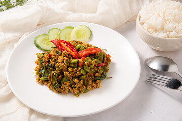 southern stir-fried pork with yellow curry paste decorate by red hot chilli cucumber in ceramic white dish with fork spoon and fabric for menu design or restaurant stock photo
