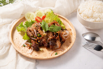 lap kor mhoo yang, spicy pork fried decorate by green salad mint cucumber tomato in wooden dish with fork spoon and fabric for menu design or restaurant stock photo