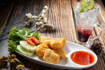 chicken nugget fry in ellipse dish fill with spicy sauce decorate by slice tomato cucumber and red soda topping mint dry flower on wood table texture stock photo morning light