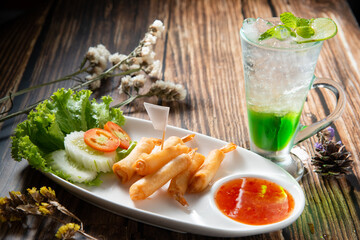 shrimp warp or ebi roll deep dry in white ellipse dish fill with spicy source decorate by slice tomato cucumber beside green soda topping mint leaf in dry flower on wood table texture, trepezoid flag