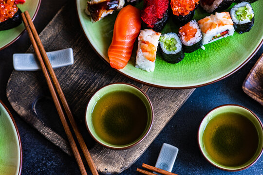 Plate of assorted maki sushi rolls and nigiri sushi on a table with green tea