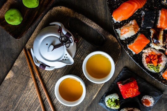 Plates of assorted maki sushi rolls and nigiri sushi on a table with green tea