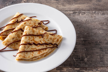 Sweet crepes with chocolate on wooden table.	Copy space