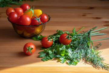 Cherry tomatoes red and yellow in a vase on a table with parsley and dill