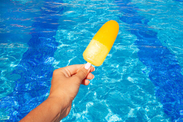Hand holds yellow ice cream on the background of the pool. Summer concept, vacation