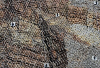 Wire netting and bolts containing a rock face.