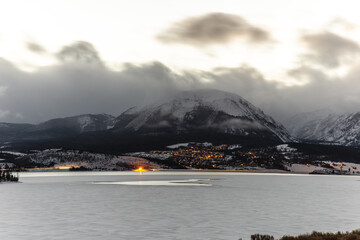 view of a mountain on the other side of the lake in winter with dark clouds on a sunset