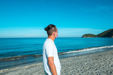 A man during the coronavirus pandemic on the beach looking at the sea with a surgical mask