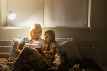 Family bedtime. Mom and child daughter reading a book in bed