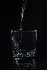 Water pouring into glass on dark background
