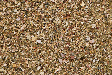 Beach sand texture. Broken seashells background. Colorful sand surface of a beach with clear sea water.