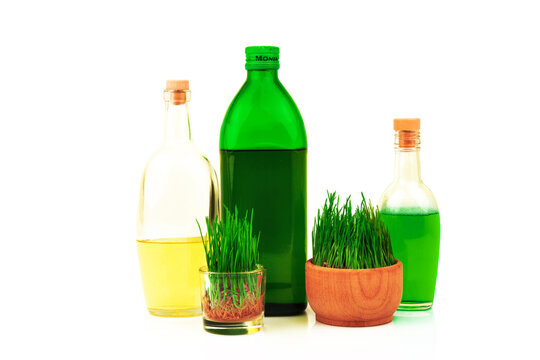 Glass bottles with oil and juice and sprouts of wheat in wooden bowl isolated on white background