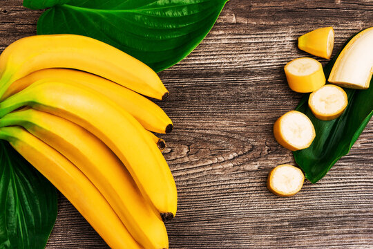 Bunch of raw organic yellow bananas with slices and green leaves on wooden background