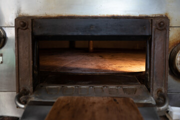 Wooden shovel set in front of a stone oven open door