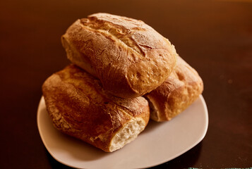 Pan ciabatta servido en una mesa de madera.  Pan recien horneado. Pan sobre plato de porcelana blanca

