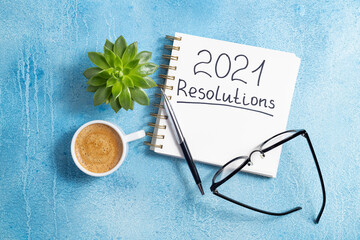 Naklejka premium New year resolutions 2021 on desk. 2021 goals with notebook, coffee cup and eyeglasses on blue background. Goal, plan, strategy, action, idea concept. Top view
