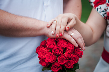 Obraz na płótnie Canvas hands of newlyweds with wedding rings on a bouquet of red roses