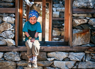 Young Sherpa Girl with Bandana Headband Sits on the window frame of under construction house and smiles at the camera in remote Manaslu region of Nepal. selective focus - obrazy, fototapety, plakaty
