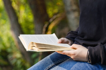 Girl reads a book close-up outdoor The background is blurred.