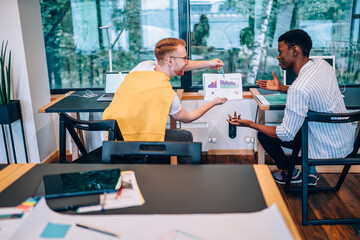 Cheerful office worker showing charts to puzzled black colleague