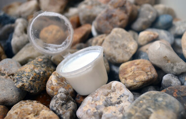 An open jar of white cream for body and face care against a background of sea stones.