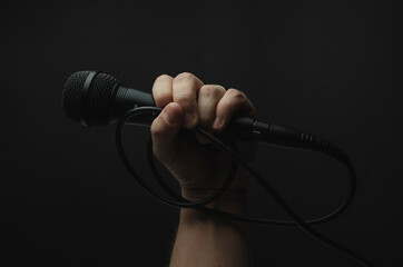 mano sosteniendo micrófono color negro con fondo color negro liso