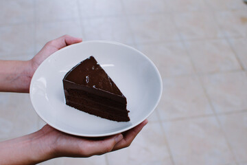 Hand holdings homemade dark chocolate cake in white plate.
