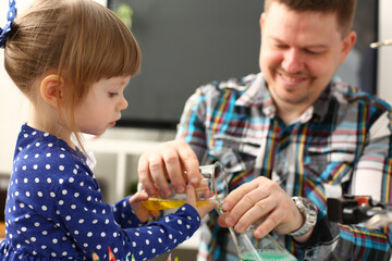 Man and little girl play with colourful liquids portrait. Young team clean research equipment...