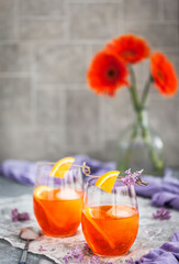 Orange Aperol Spritz cocktail served in a wine glasses, decorated with slice of orange and lilac