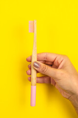 mano sosteniendo cepillo de diente de bambú color rosa con fondo liso color amarillo  