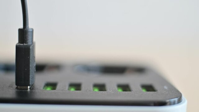 Modern convenient multi-port usb charger for devices. Close-up of a female hand plugging multi-colored cables into a power outlet. Macro.