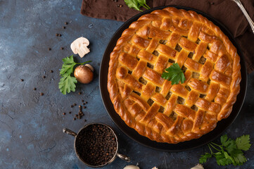 Pie with mushrooms on blue background. Homemade pie. Best for your dinner. Cooking together. Tasty meal. Pie with fresh mushrooms on a dark plate. Black pepper and green parsley for your enjoyment.