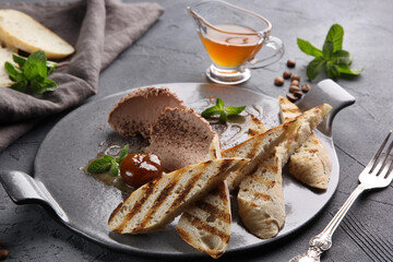 Croutons with liver pate and honey on a gray plate on a gray background in a restaurant. Next to a fork, mint and coffee. High cuisine. Background image, copy space