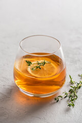 Hot tea in a glass with lemon and thyme on a gray background with copy space, side light. Autumn and winter traditional drinks.